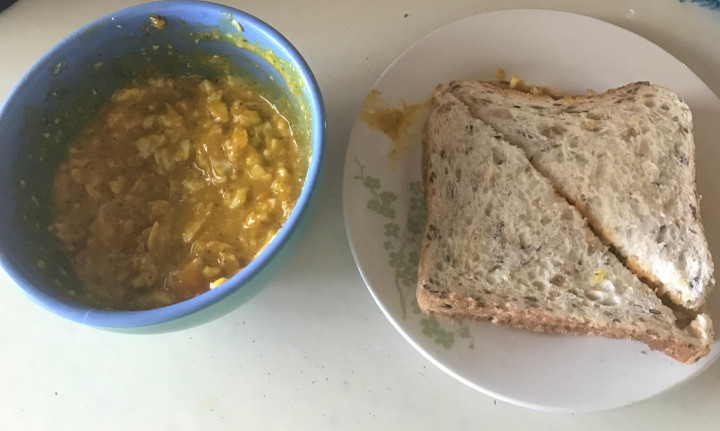 Curried eggs in a bowl and on a multi-grain sandwich.